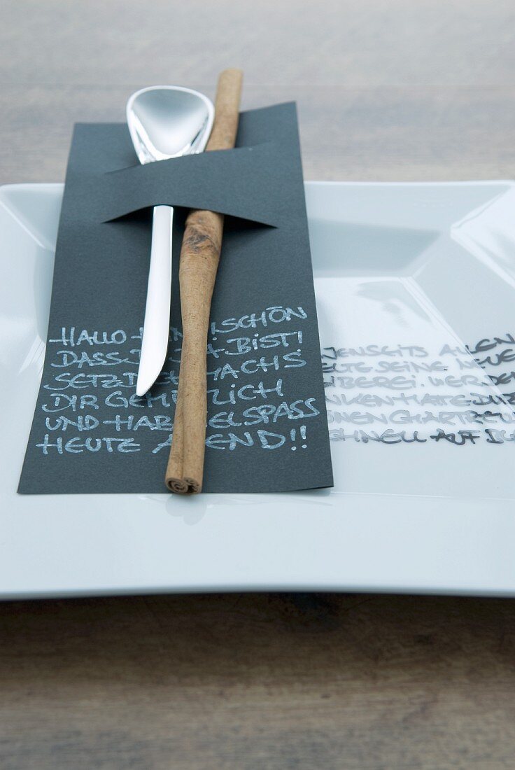 Löffel und Zimtstange in schwarzem Papier mit Botschaft auf weißem beschriftetem Teller