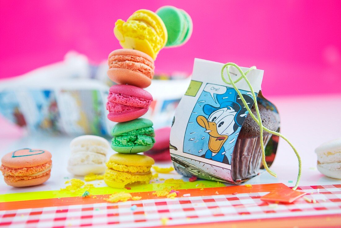 Table decorated for child's birthday party with Donald Duck comic pages and stack of colourful macaroons against pink background