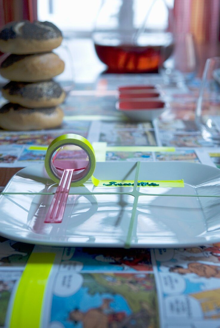 Gummi verspanntes Gedeck mit Plastiklöffel und Kleberolle als Tischkarte auf Comic Tischdecke