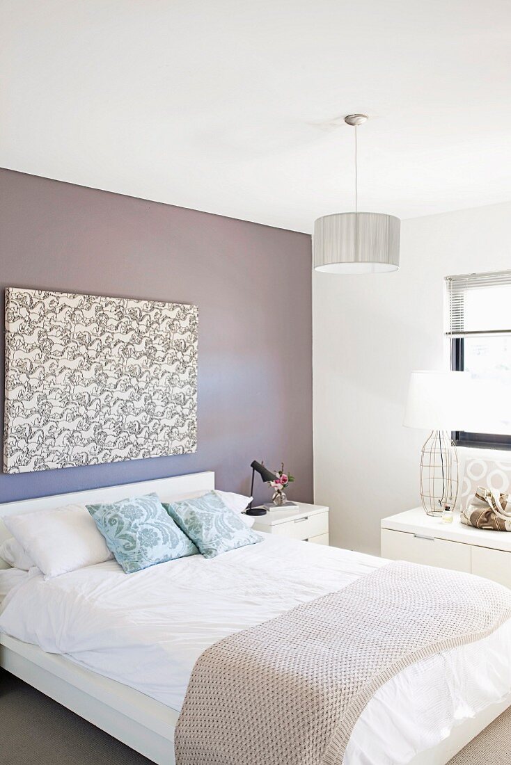 Doppelbett mit Tagesdecke vor hellgrau getönter Wand und modernem Bild in schlichtem Schlafzimmer