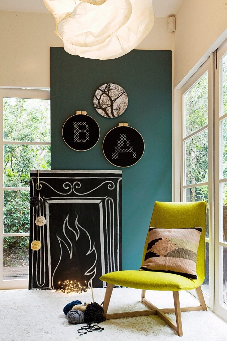 Selbstgemachtes stilisiertes Kaminfeuer aus Holzplatte, Tafelfarbe, Kreide und Lichterkette in gemütlicher Sitzecke mit Stuhl & Stickrahmenbildern an der Wand
