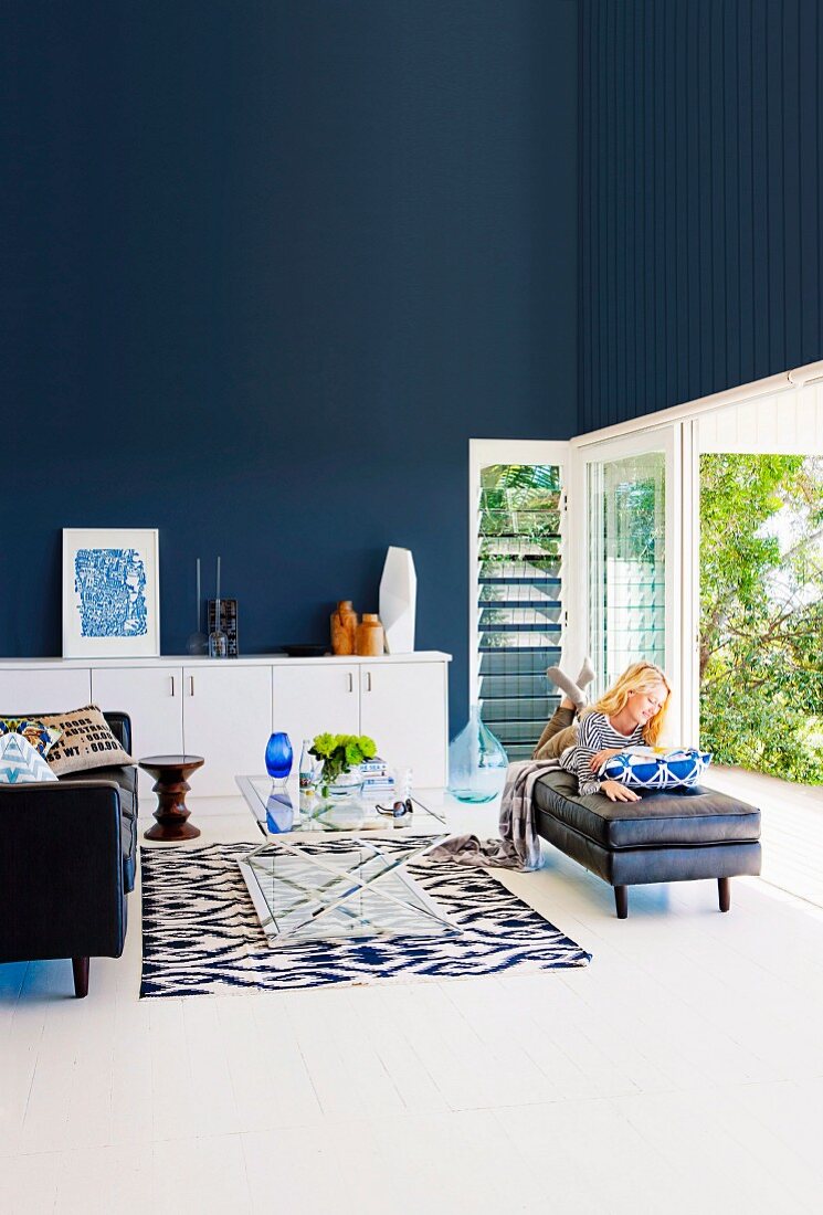 Elegant living room with dark blue wall, woman reading in front of an open terrace door