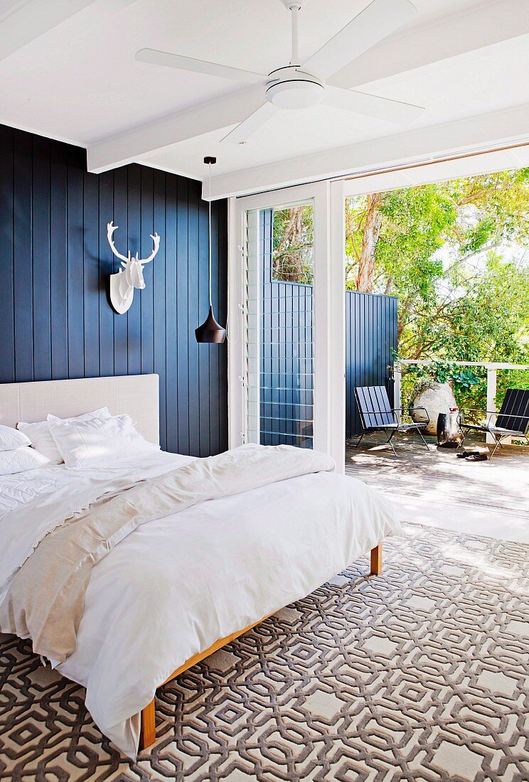 Bedroom with graphic carpet pattern, black wall covering and white stylized trophy in front of the terrace