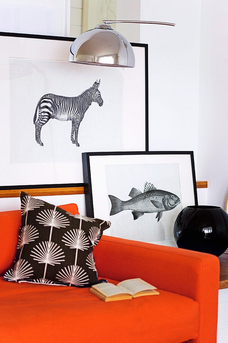 Schwarz gerahmte Tiergrafiken hinter orangefarbenem Sofa