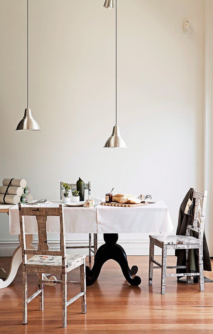 Hängeleuchten mit schlichtem Metallschirm über selbstgebautem Tisch aus alter Tür und Küchenstühle mit Zeitungspapier beklebt