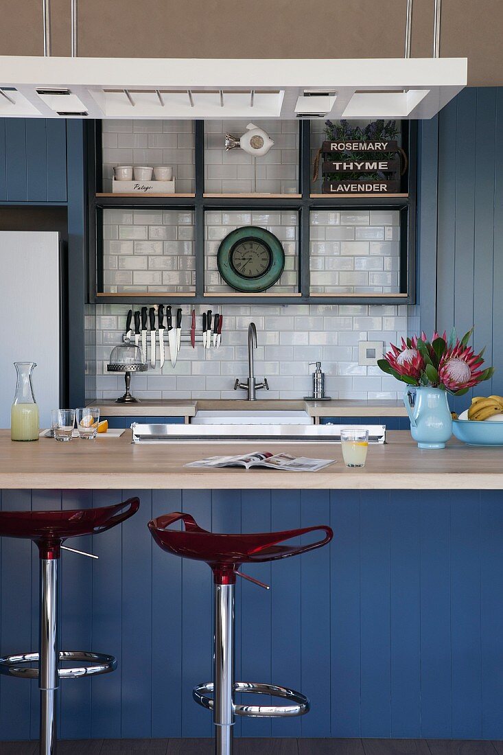 Blau lackierte Küchentheke mit Designer Barhockern, im Hintergrund Einbauküche mit weiß gefliestem Spritzschutz