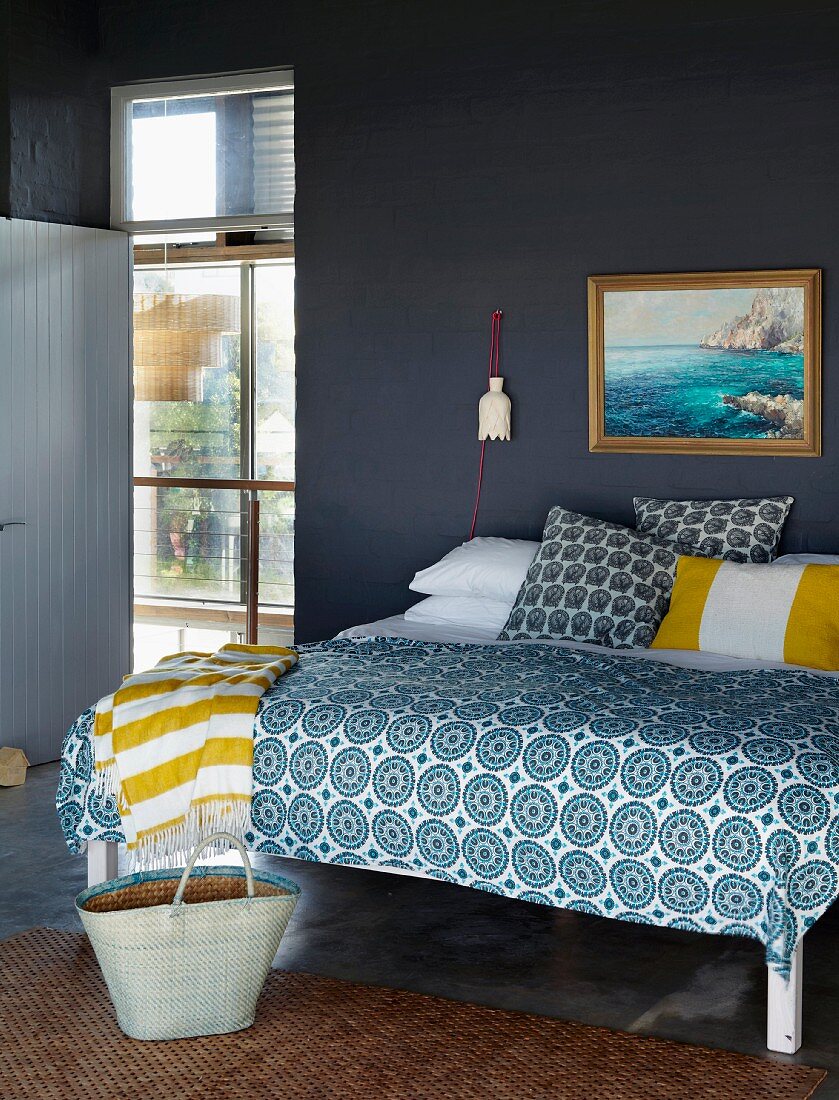 Double bed with blue and white patterned bedspread against brick wall painted dark grey and view into bright hallway