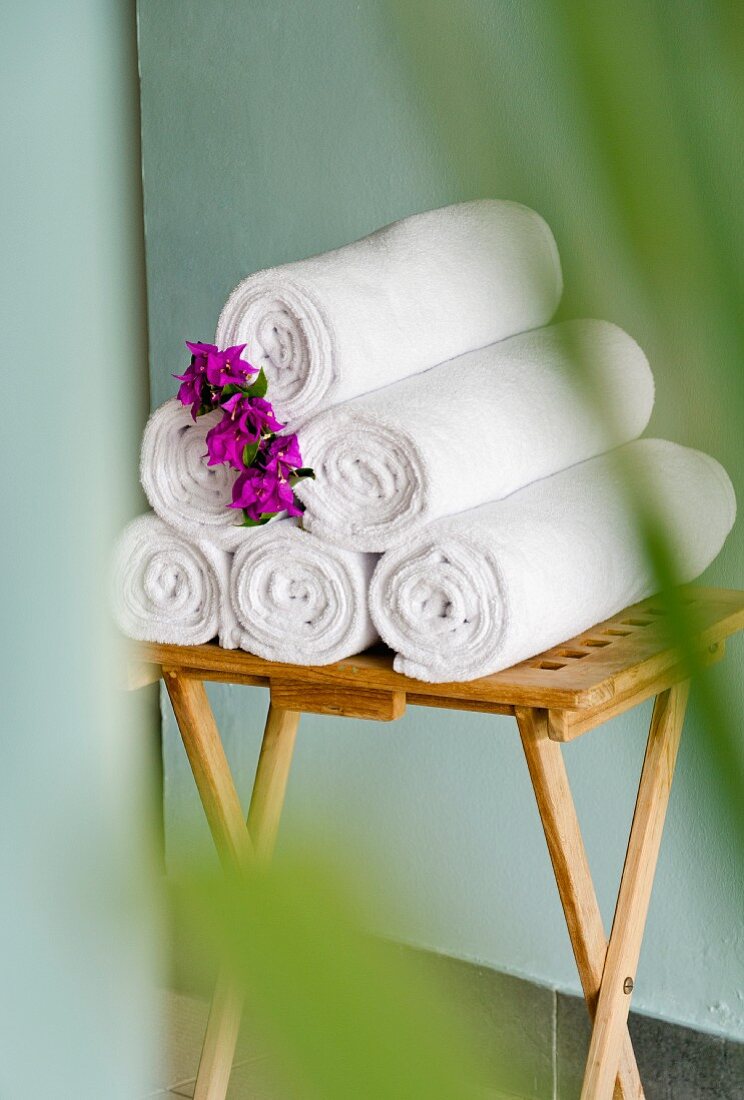 Rolled bath towels decorated with flowers on a small, wooden table