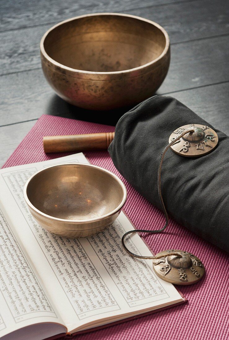 Tibetan bowls, cymbals and an open book in sanskrit on a pink yoga mat