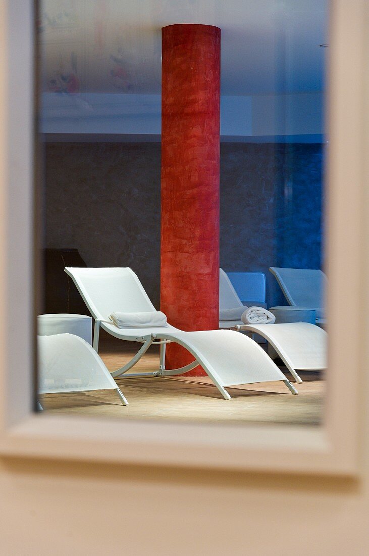 Liegestühle und rot marmorierte Betonsäule mit Spiegelreflexion im Ruheraum eines Spas