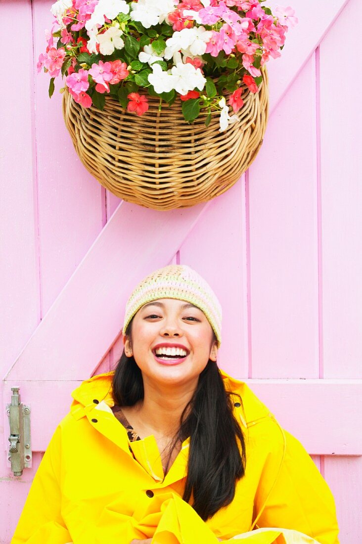 Lachendes Mädchen vor rosa Holztür unter prachtvoller Blumenampel