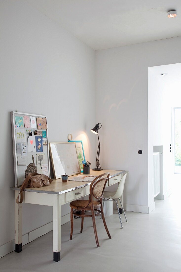 Nostalgischer Arbeitstisch mit Schreibtischlampe, zwei unterschiedlichen Stühlen und an die Wand gelehnte Pinnwände