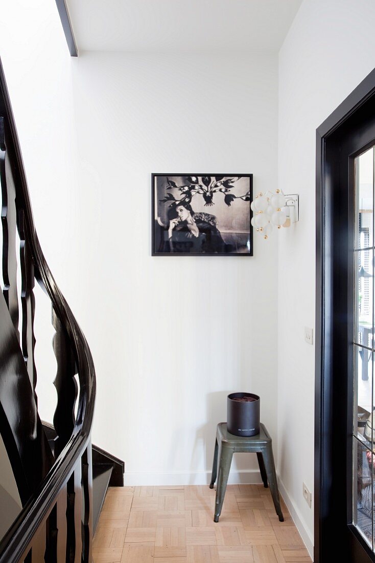Klassiker Hocker aus Metall mit Behälter in Ecke eines Treppenhauses, an Wand gerahmtes, schwarzweiss Photo