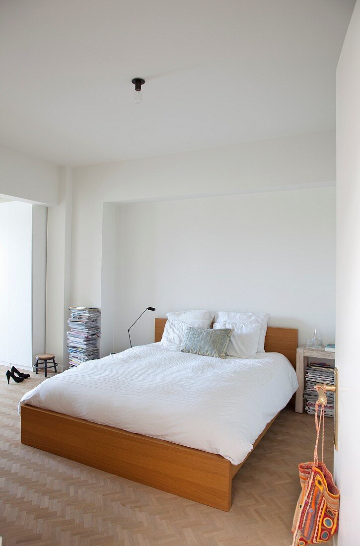 View through open door of double bed with wooden frame on herringbone parquet floor in minimalist bedroom