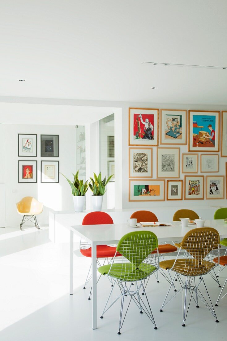White dining table, wire chairs with colourful upholstery and gallery of artworks in light-flooded, open-plan living area