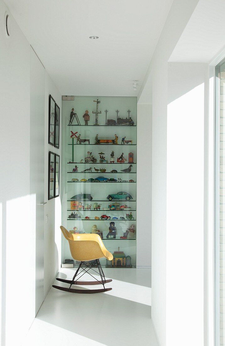 Eames-Schaukelstuhl vor antikem Spielzeug hinter Glastür im hellen Flurbereich