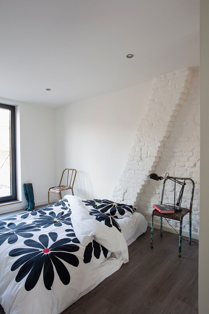 Schlichtes Bett mit geblümter Bettwäsche und Retro-Metallstühlen in minimalistischem Schlafzimmer