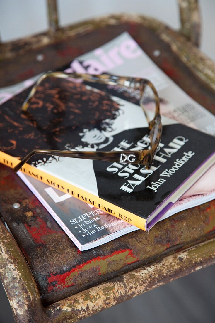 Lesebrille und Buch auf Metallstuhl mit abblätternder Farbe