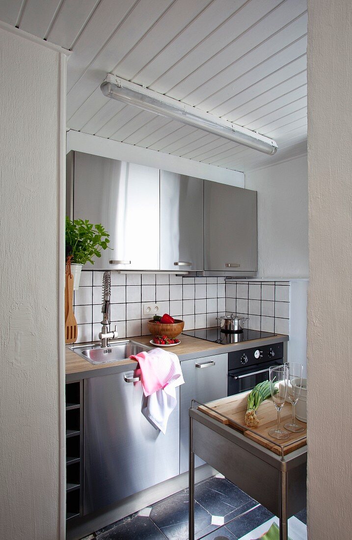 View into kitchen with stainless steel doors, white tiled splashback and white-painted wooden ceiling