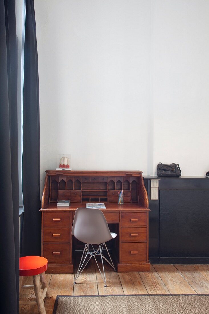 Antiker Sekretär mit grauem Eames Chair in Zimmerecke einer renovierten Altbauwohnung