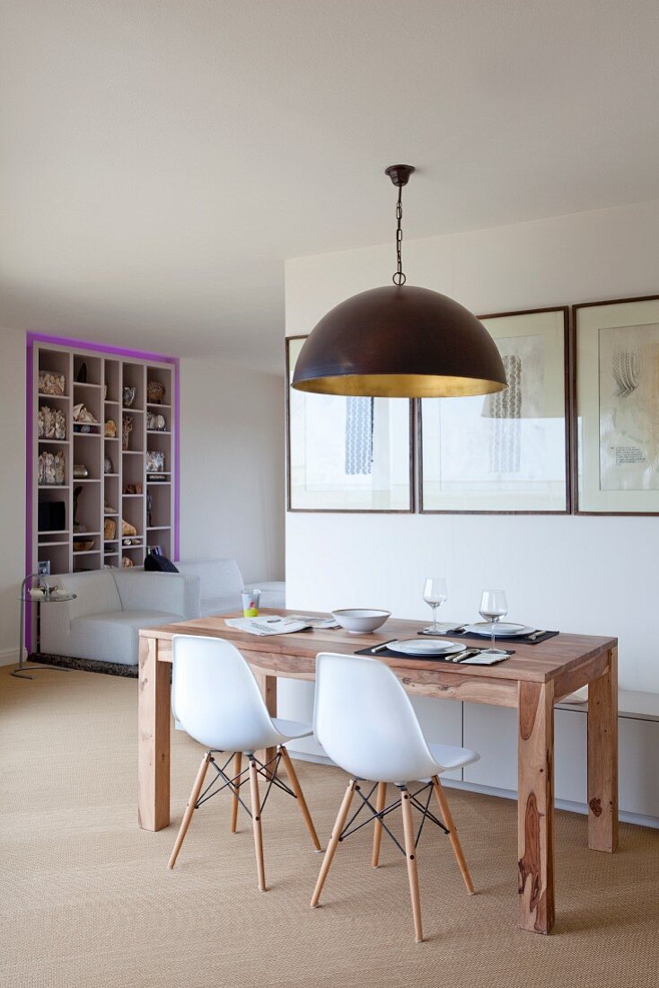 Open-plan kitchen with wooden table and white designer chairs below black pendant lamp