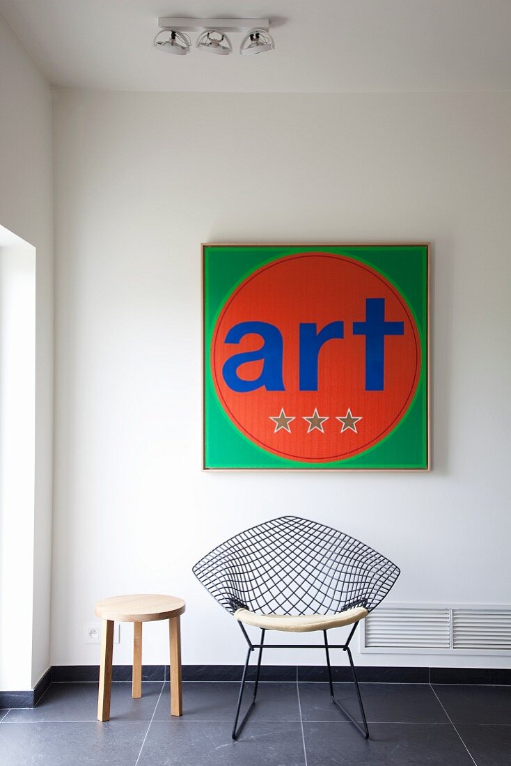 Bright, square, modern artwork with lettering and Eames Wire Chair on dark tiled floor