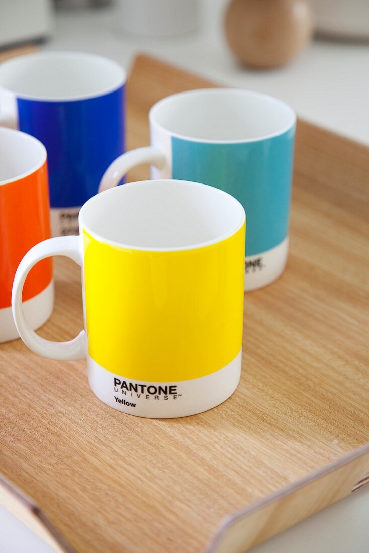 Vier farbenfrohe Tassen auf Laminattablett mit Holzmaserung
