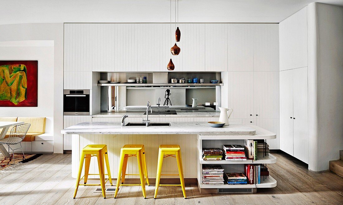 weiße Einbauküche mit verspiegeltem Spritzschutz, Kücheninsel mit Marmor Arbeitsplatte und gelben Retro Barhockern