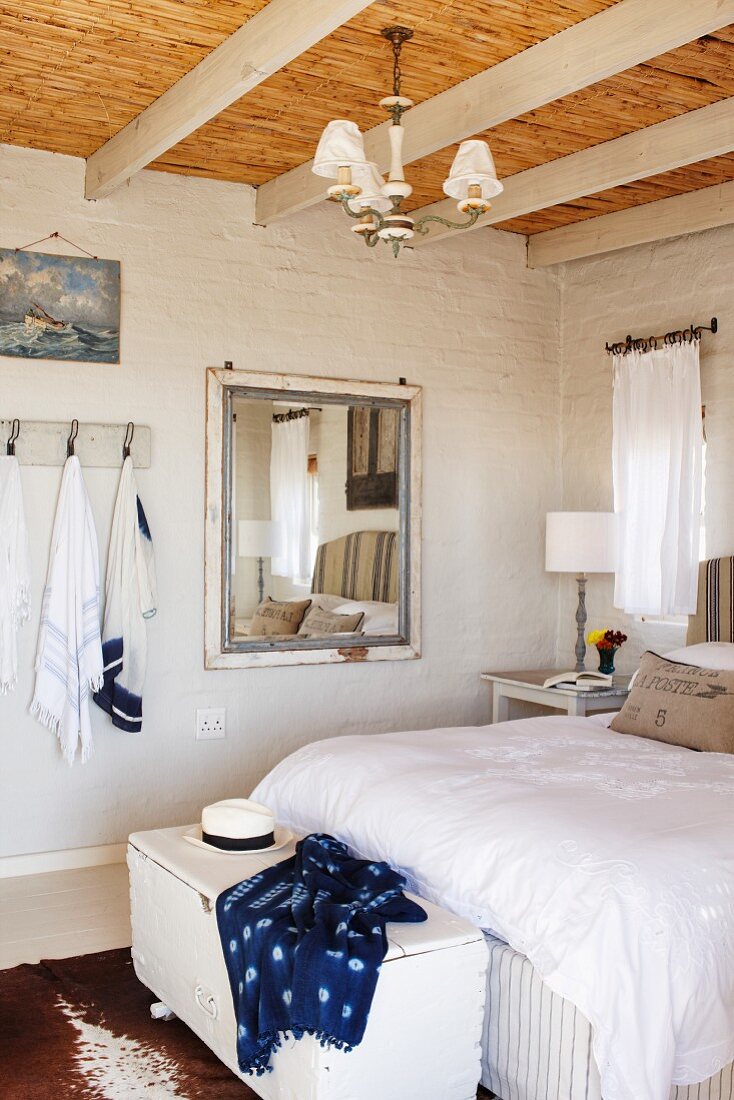 weiße Truhe an Bettende eines Doppelbettes mit weisser Bettwäsche im Schlafzimmer mit Holzbalken und Bambusdecke