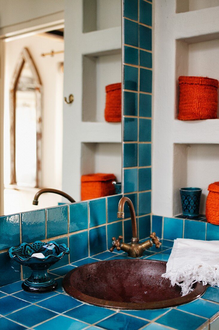 Blue tiled washstand with built in metal basin and vintage tap fittings in corner of bathroom