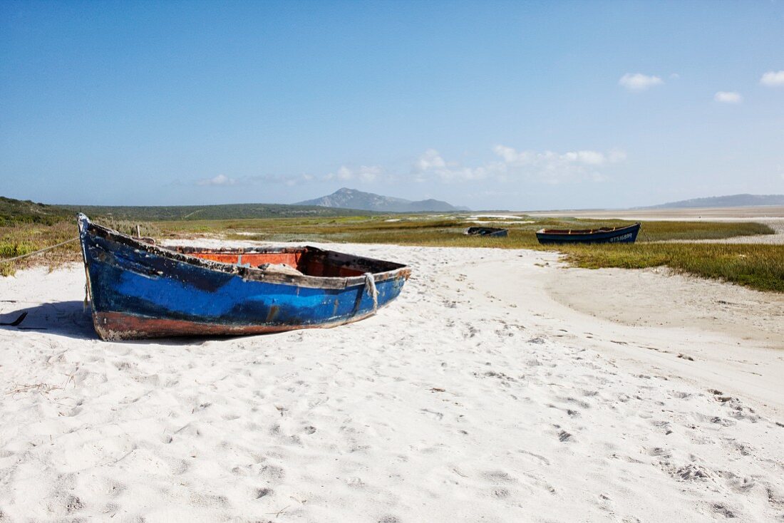 Schlichtes Boot mit blauer, abblätternder Farbe auf Sandplatz am Strand