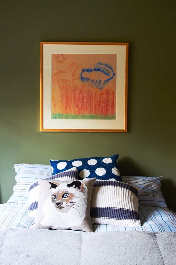 Katzenmotiv auf Kissen und gerahmtes Bild an grüner Wand im Schlafzimmer
