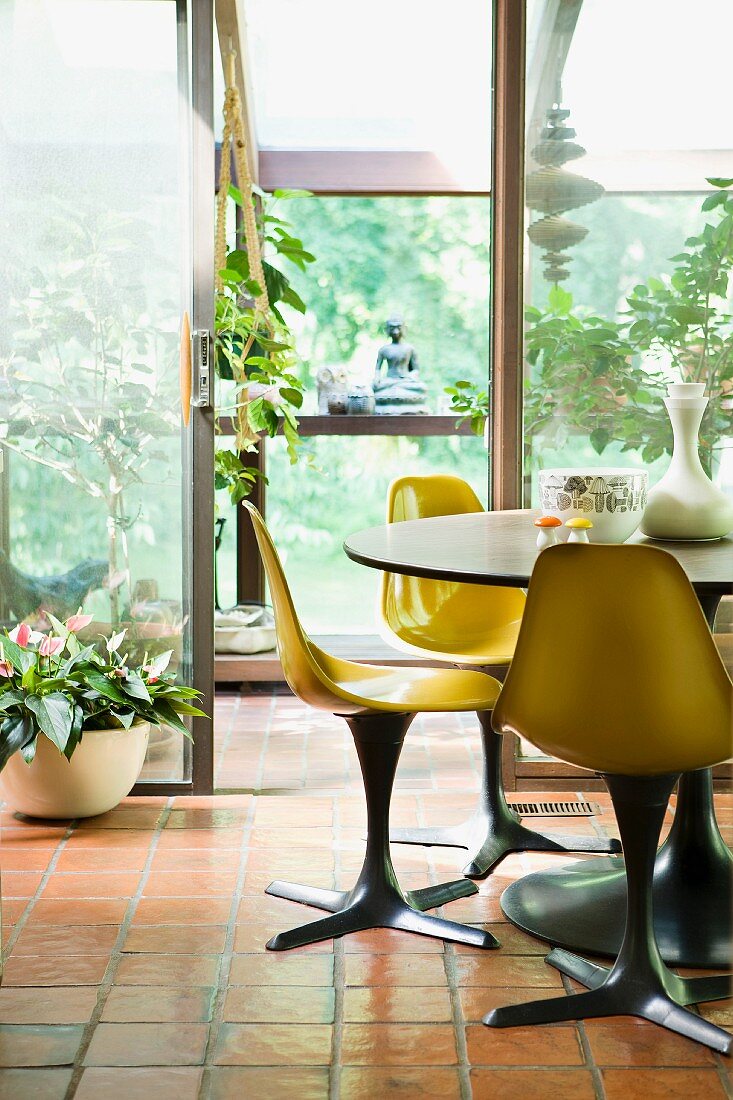 Tisch und Stühle in einem Wintergarten mit Pflanzen und Dekogegenständen aus Asien