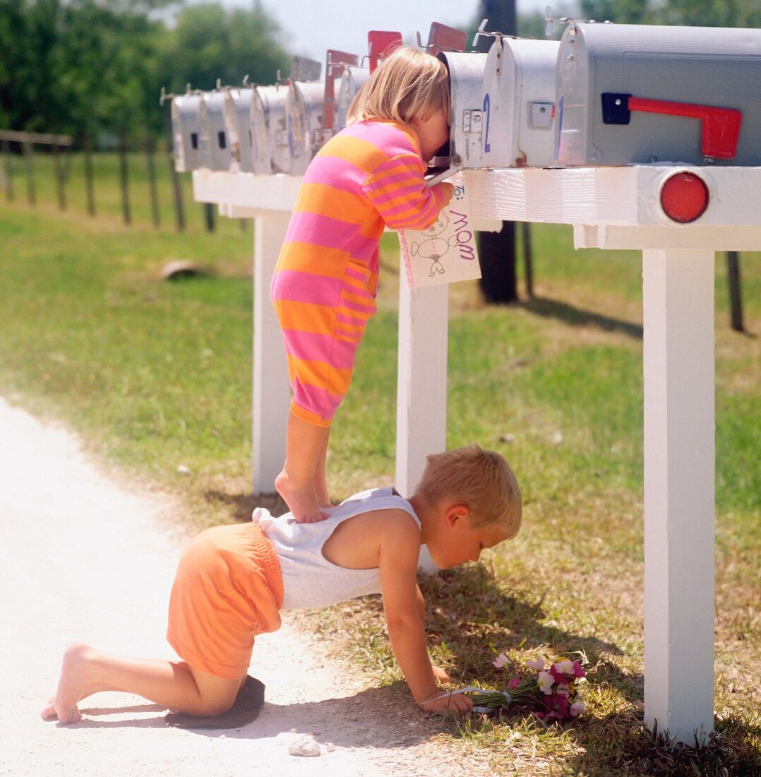 Kleines Mädchen steht auf Rücken ihres Brudern & schaut in Briefkasten