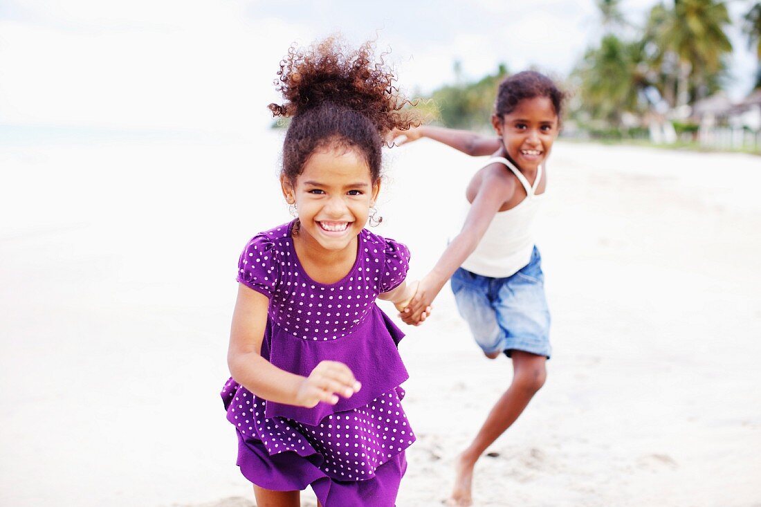 Zwei dunkelhäutige Mädchen laufen Hand in Hand am Strand entlang