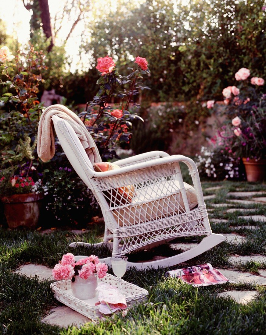 White, wicker rocking chair in romantic rose garden
