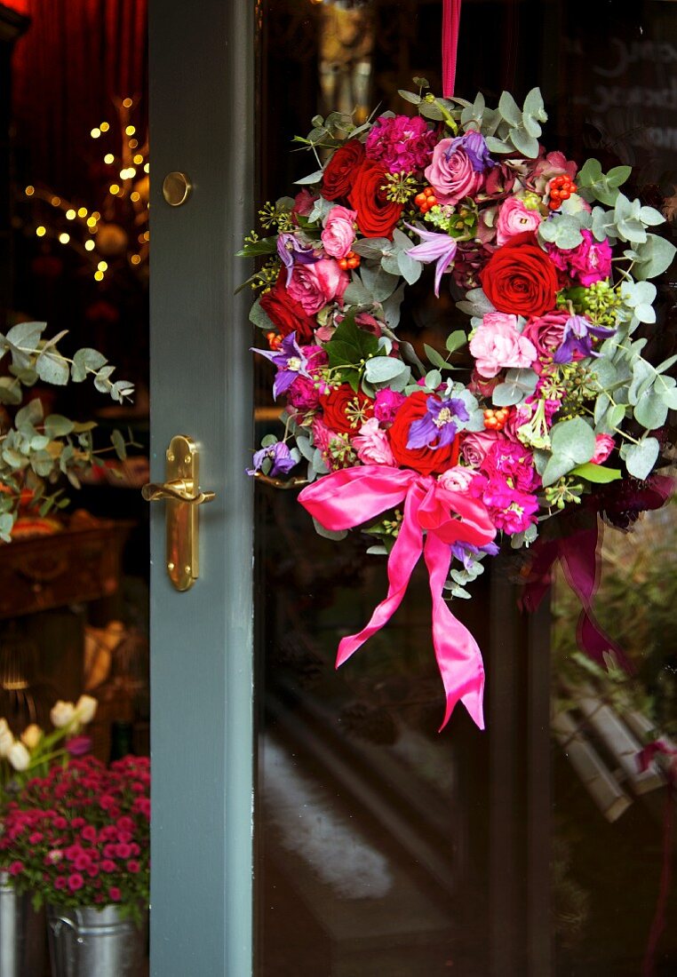 Blumenkranz in verschiedenen Rot- und Pinktönen an Glastür mit Messingbeschlag