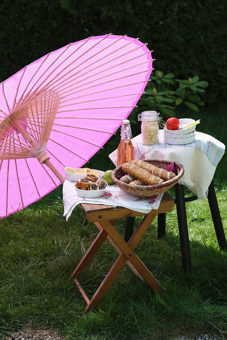 Picknick mit Laugenstangen und Limonade unter asiatischem Papierschirm im Garten