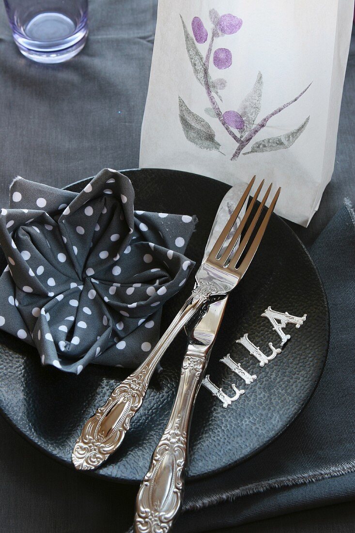 Tischgedeck: Serviette als Lotusblume gefaltet, Teelicht in transparenter Tüte und Buchstaben auf Teller