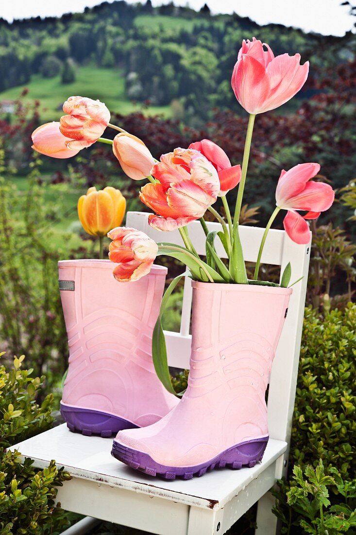 Rosa Gummistiefel auf Gartenstuhl mit Tulpen
