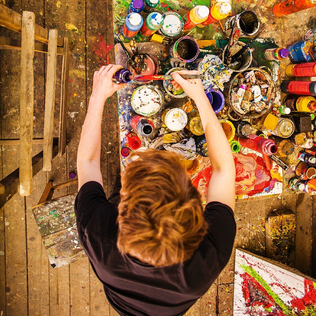 Vogelperspektive auf jungen Künstler an Tisch mit Farbtöpfen in einem Maleratelier