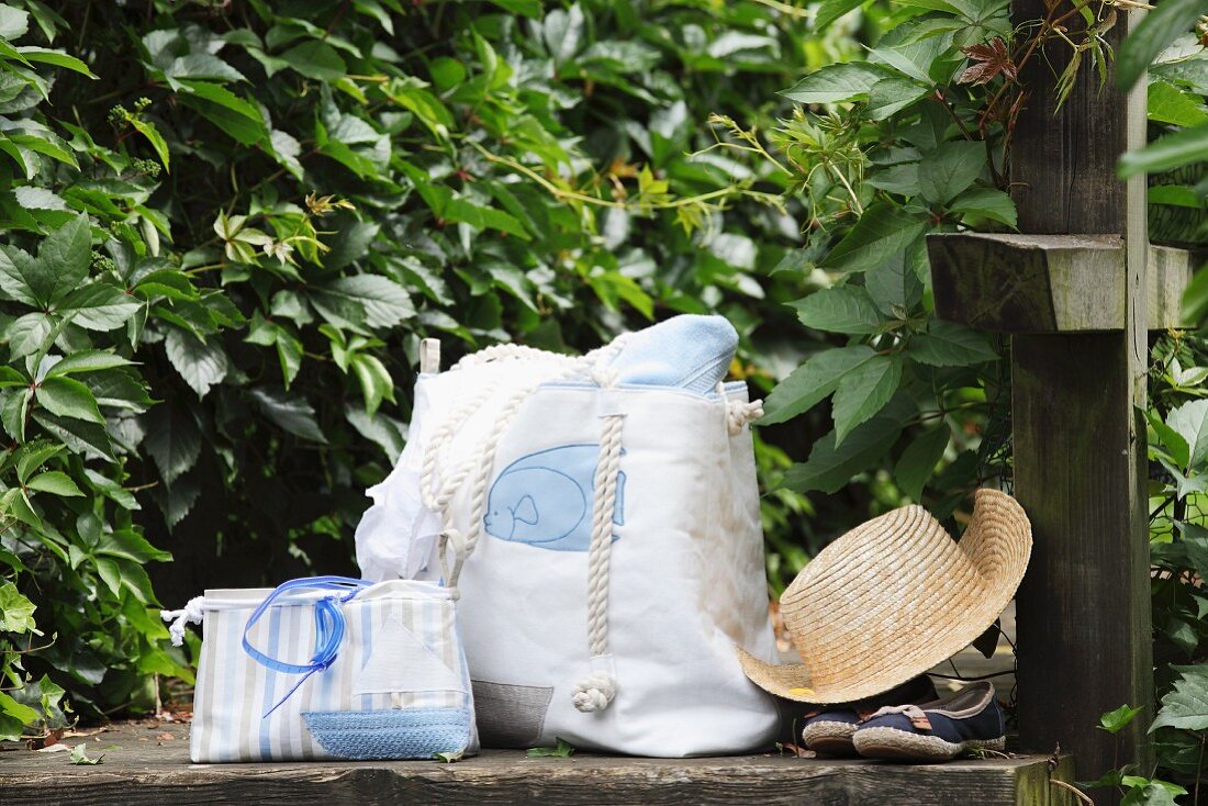 Hand-sewn beach bag and cosmetics bag next to straw hat on stone wall in garden