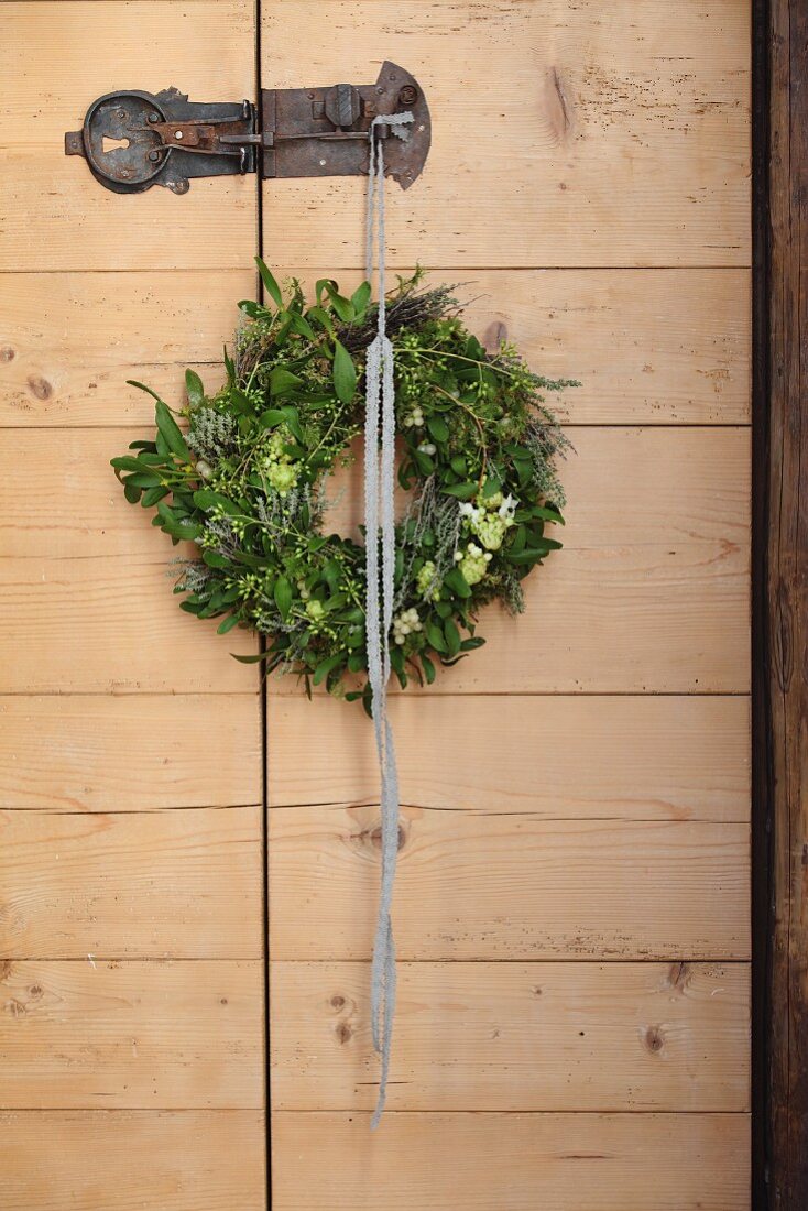 Rustic wooden door with wreath of mistletoe and Star-of-Bethlehem hanging from wrought iron latch