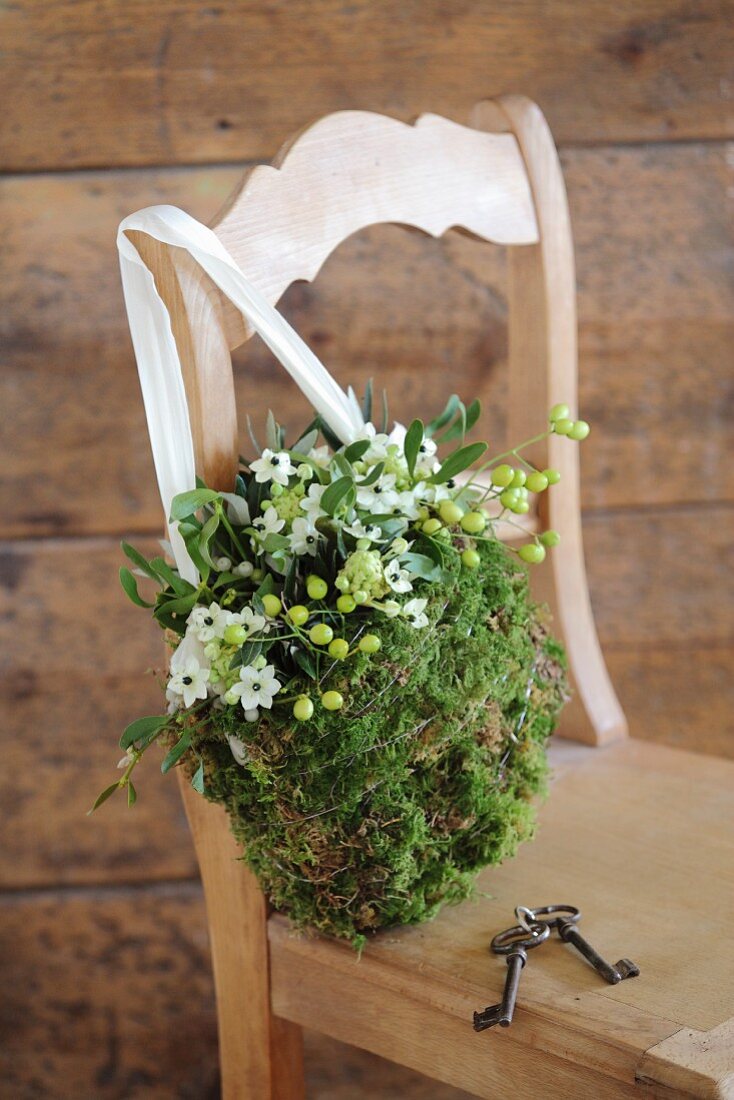 Romantic, bag-shaped arrangement of moss, mistletoe and Star-of-Bethlehem on wooden chair