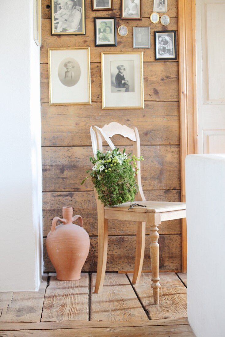 Romantischer Blütenbeutel aus Moos, Misteln und Milchsternen an Holzstuhl, darüber Bildergalerie an Holzwand