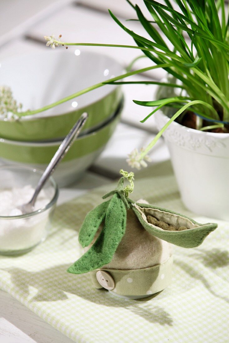 Eierwärmer mit gefilzten Zuckerschoten geschmückt auf zart grün-weiß kariertem Tischset