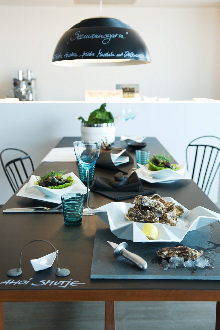 Stilvoll gedeckter Tisch mit Austern in weißem Designer Porzellan und blauen Trinkgläsern