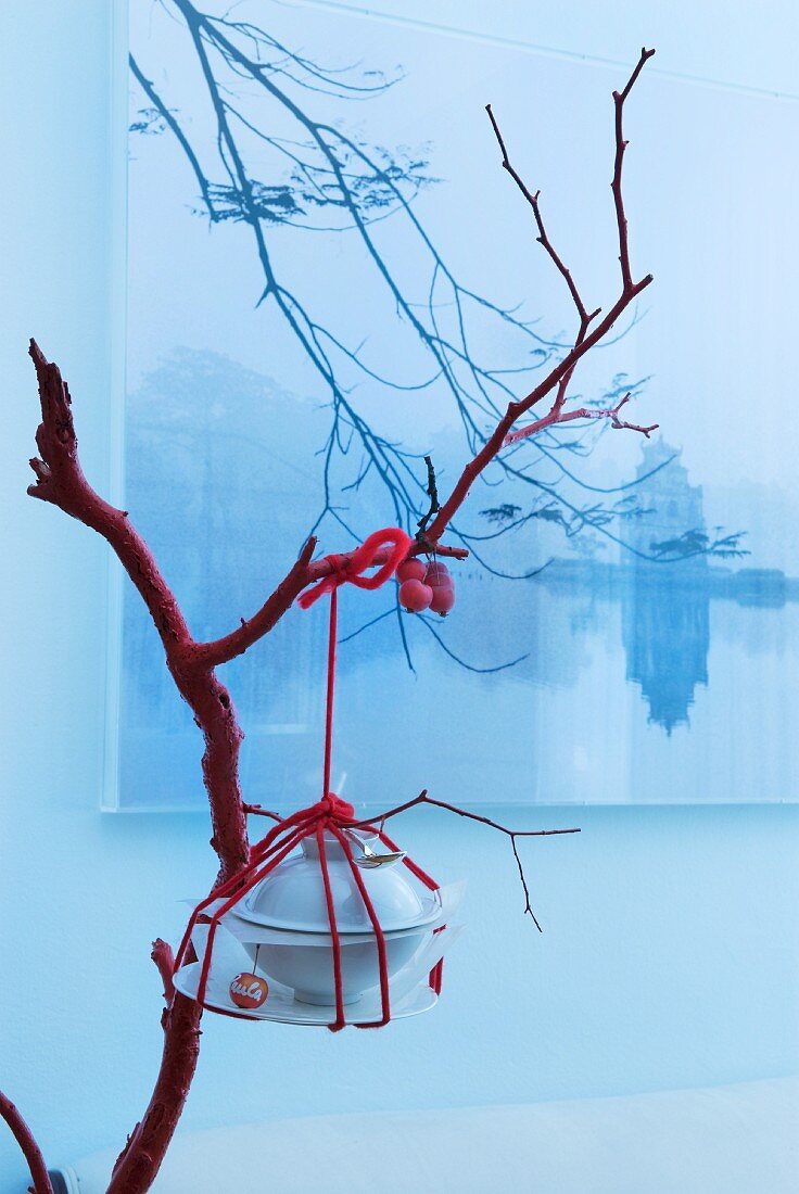 Oriental table decoration: crockery and cutlery wound around with red wool hanging from branch