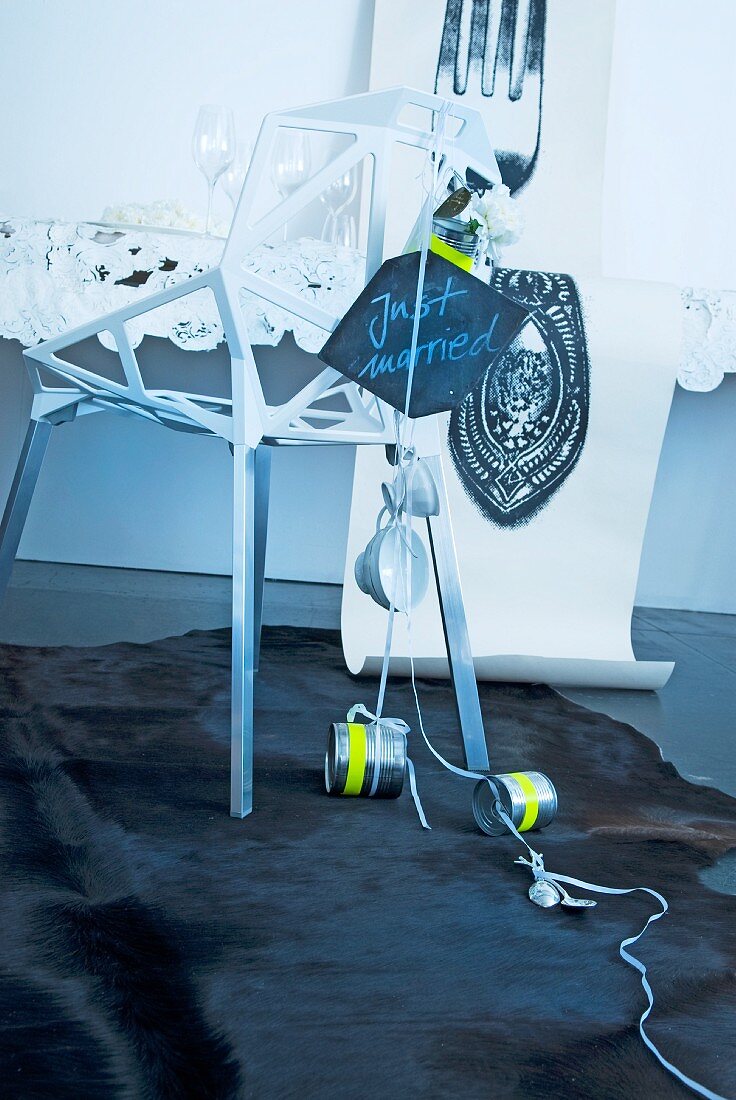 Unkonventionelle Dekoration für ein Hochzeitsbankett - Designer Stuhl aus weißem Metallgitter behängt mit Hochzeitsschild, Tassen und Dosen vor dem Tisch