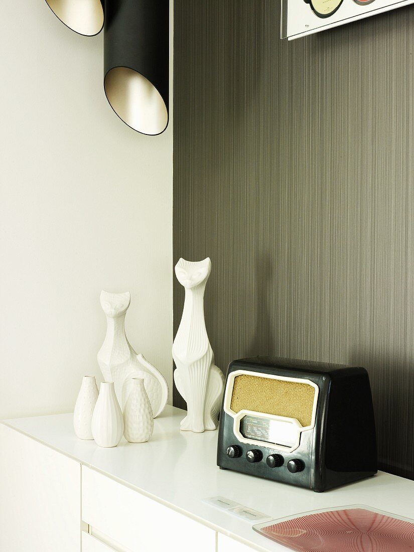 Fifties radio next to white ceramic vases and cat figurines on sideboard